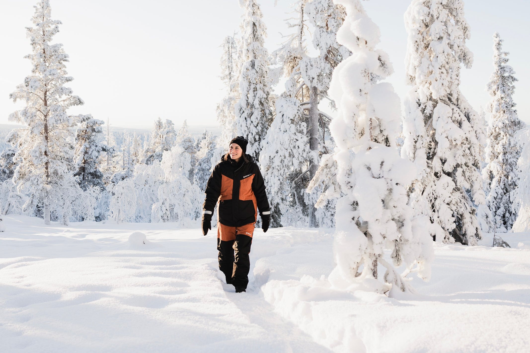 Person wearing insulated winter clothing walking through a snowy landscape with snow-covered trees